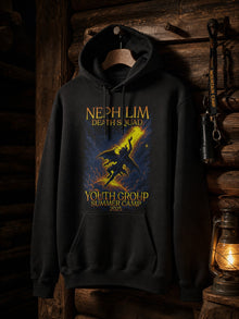 Black Nephilim Death Squad Youth Group Summer Camp 2025 hoodie hanging on a wooden peg in a dark camp cabin by lantern light