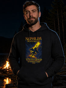 Man wearing the black NDS Youth Group Summer Camp 2025 hoodie beside a lakeside campfire at night