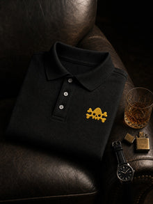 Black Nephilim Death Squad embroidered logo polo with the yellow skull on the left chest, styled on a leather armchair with a watch and whiskey glass