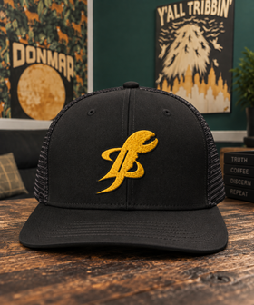 Black TopLobsta trucker hat with yellow embroidered claw logo on a dark wood table
