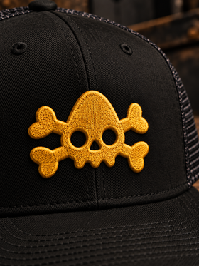 Close-up of yellow embroidered NDS skull logo on black trucker hat