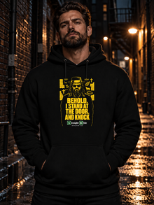 Man wearing black Behold, I Stand at the Door Hoodie by Straight Bible, yellow Jesus figure with Hebrew YHWH and Shalom