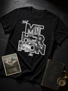 Black Visit Mt. Hermon 1 Enoch travel-poster parody T-shirt styled flat lay with a vintage mountain postcard, old book and compass